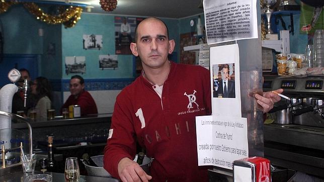 Rafael Le�n posa en su bar, donde se sigue fumando, junto a carteles de protesta con la imagen de Zapatero