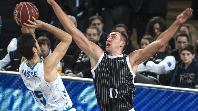 El alero belga del Bilbao Basket, Axel Hervelle (d), trata de taponar el lanzamiento del alero del Cajasol, Joan Sastre (i)